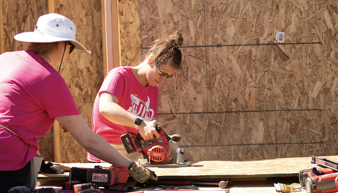 Two women working together to cut a board with a skill saw.