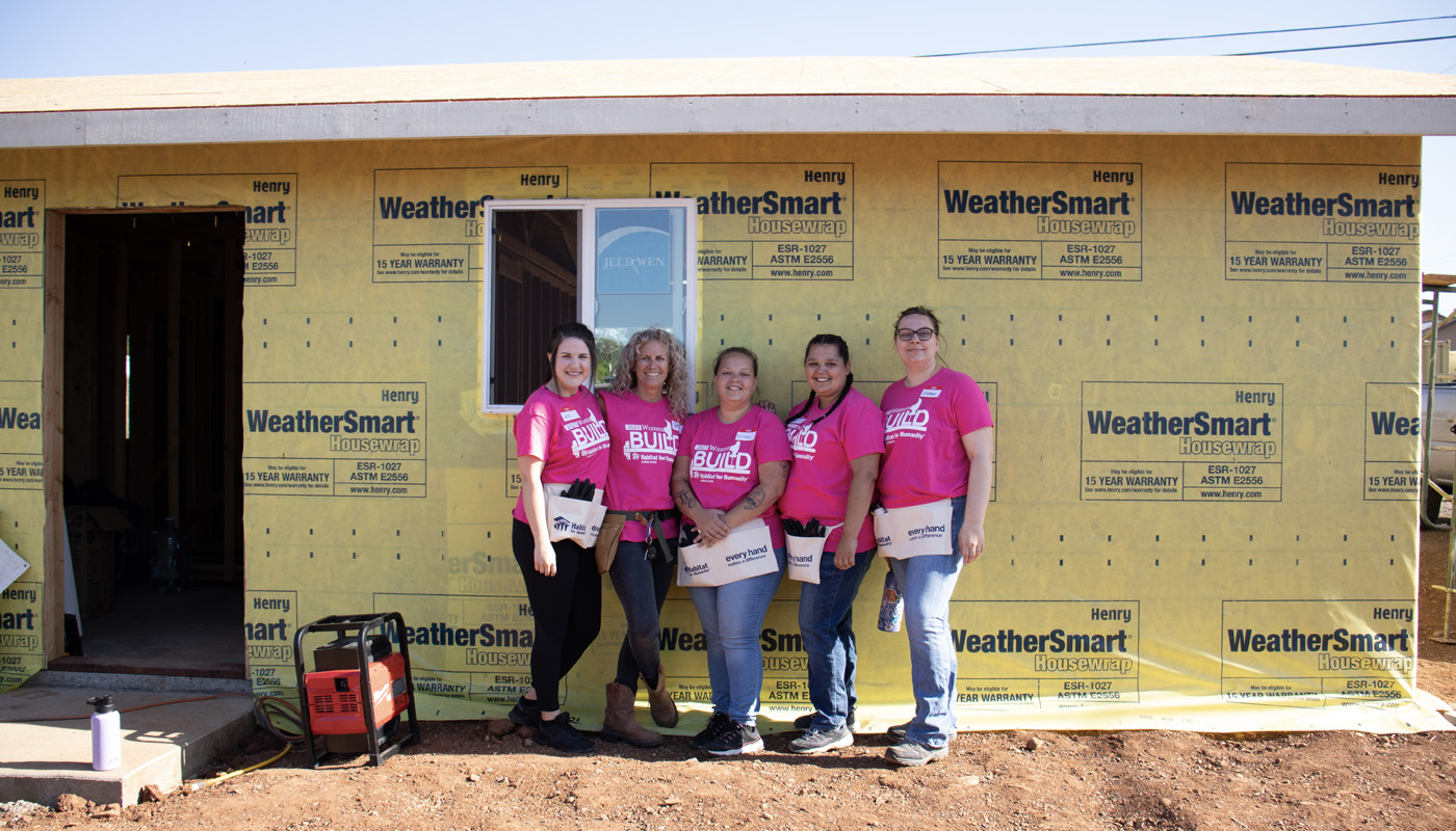 Five women volunteers standing in front of a home they're building